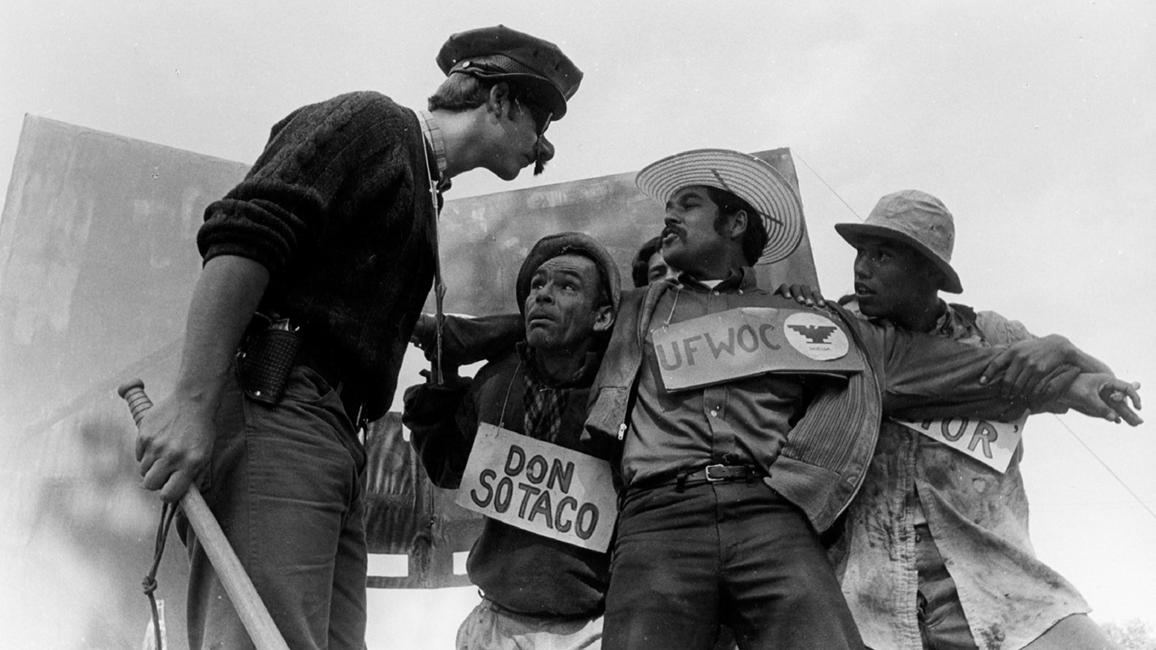 Three men wearing protest signs around neck talking to a man wearing a fake mustache 